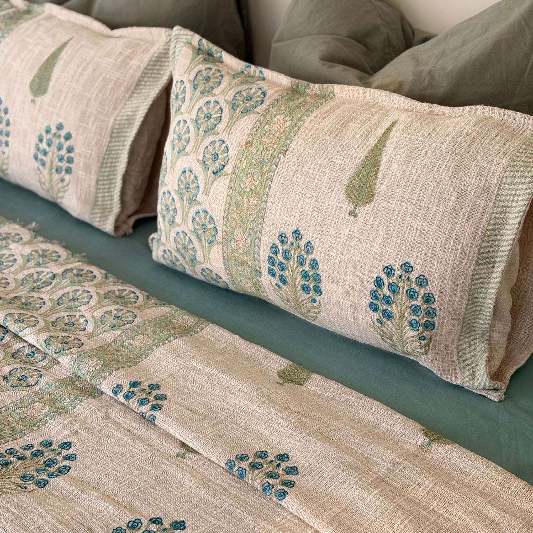 Patterned pillows and quilt on a bed with green and beige tones.